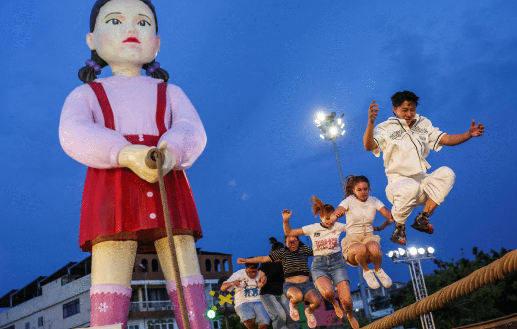 jerëzit luajnë një lojë me litar kërcimi me kukulla gjigande të quajtura 'Young-hee' dhe 'Chul-su' nga seriali i Netflix-it 'Squid Game' gjatë një eventi promovues për sezonin final të 'Squid Game 3' në Sheshin e Bashkisë në Bangkok, Tajlandë, më 30 qershor